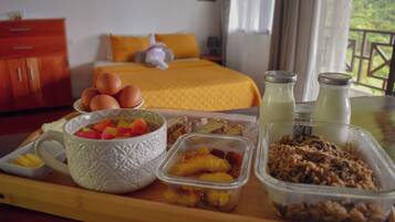 A breakfast tray with eggs, fruit, and cereal in a hotel room with a bed and a view of greenery.