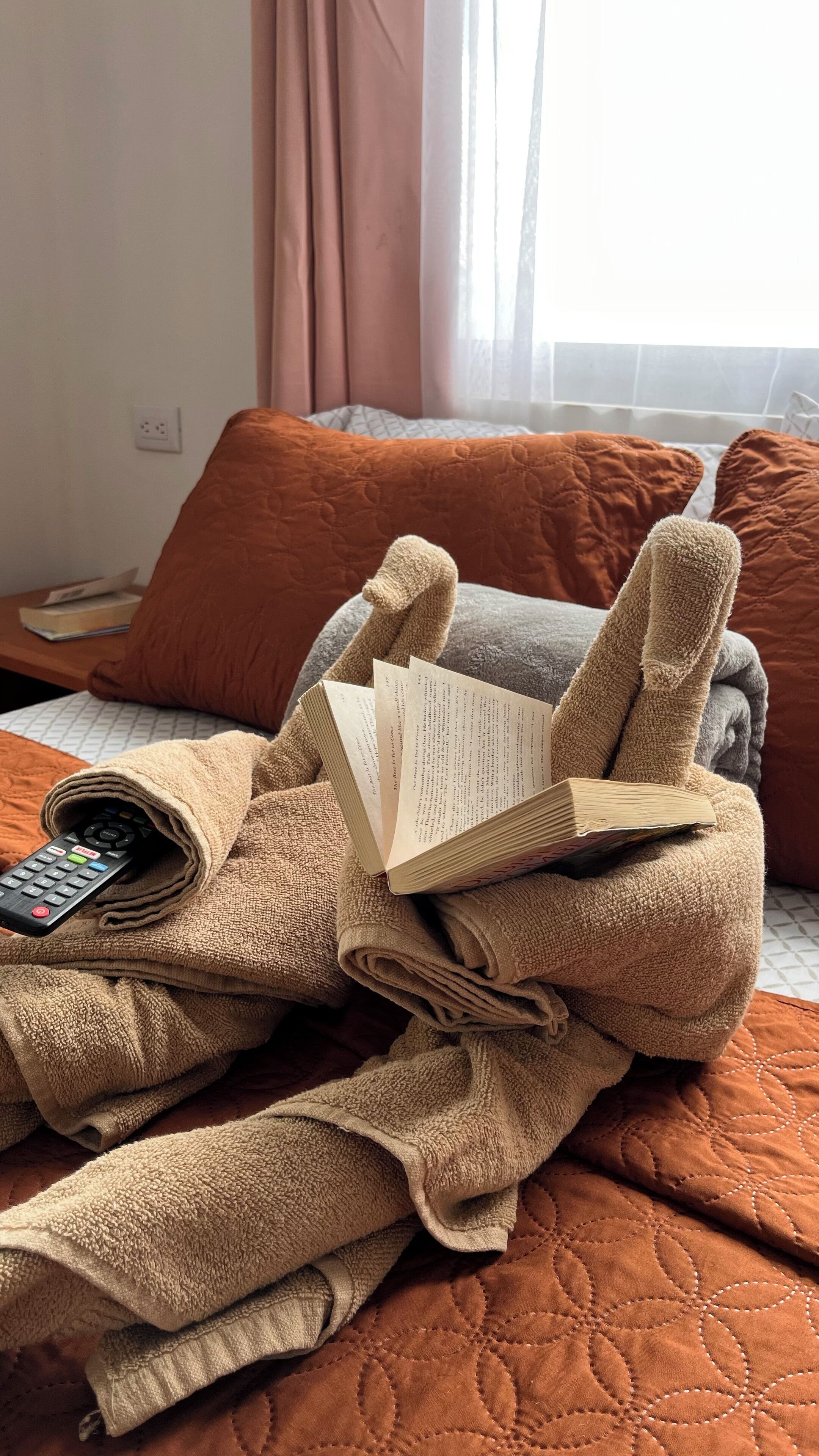 Ein Bett mit einer orangefarbenen Steppdecke, einer Fernbedienung und einem Buch.