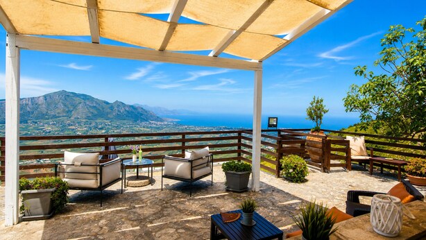 A covered outdoor seating area with a view of the sea and mountains.