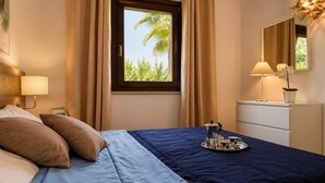 A hotel room with a bed, a bedside table with a lamp, a window with curtains, a dresser, and a tray with a coffee pot and cups.