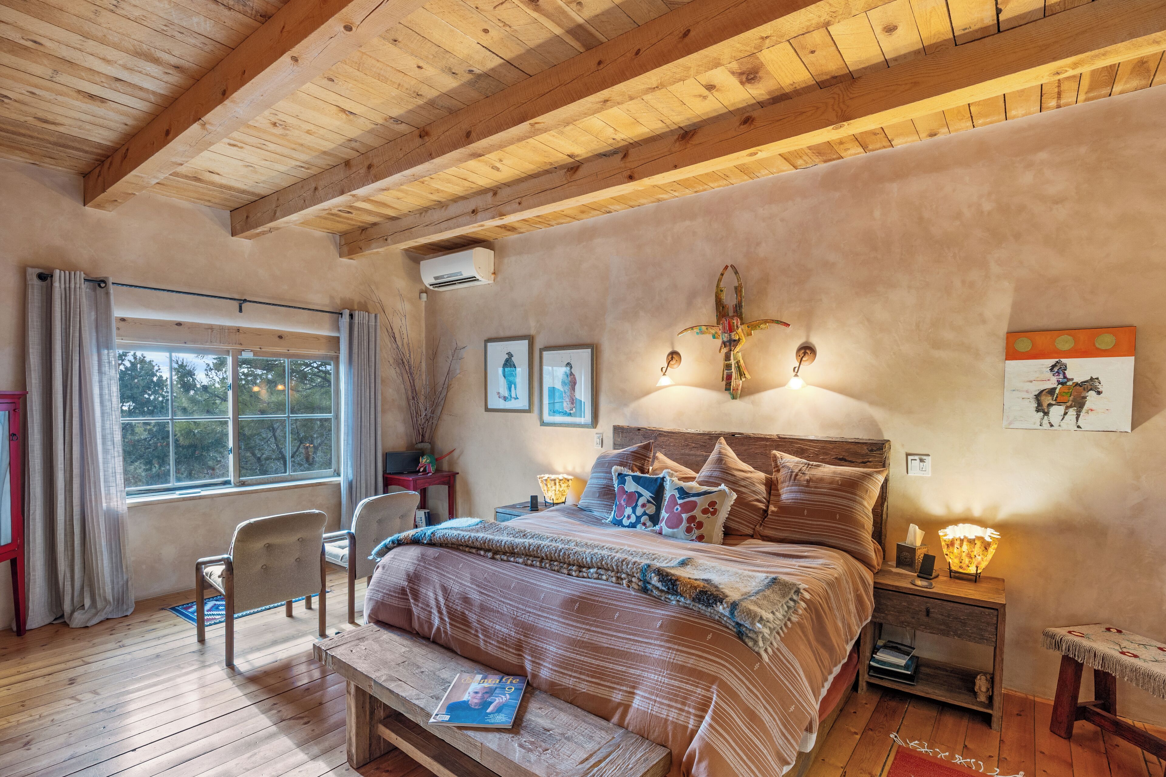 Ein gemütliches Schlafzimmer mit Holzbalkendecke, einem großen Bett mit vielen Kissen, einem Nachttisch mit Lampe und einem Fenster mit Vorhängen.