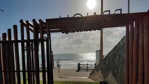 Un cancello in legno che dà accesso a una spiaggia, con un muro in pietra e un sentiero lastricato.