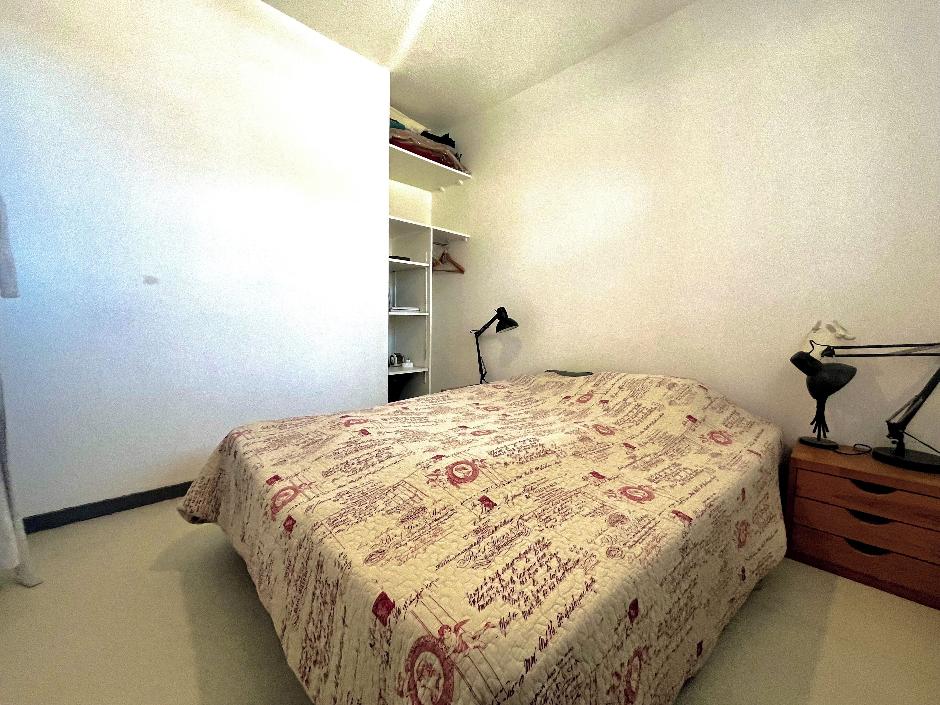 A bedroom with a bed, a desk, a lamp, and a wardrobe.