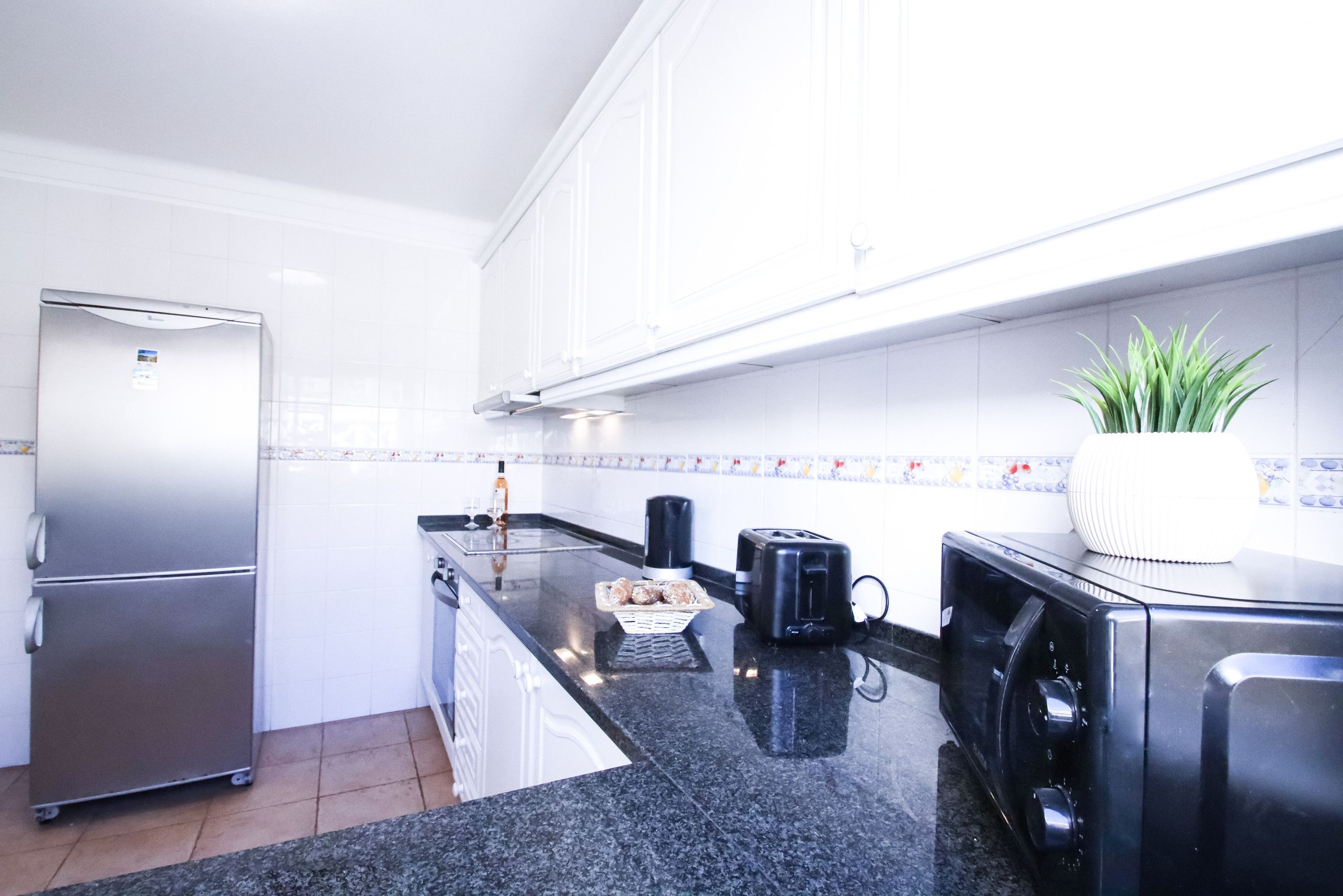 A modern kitchen with a stainless steel refrigerator, a black toaster, and a potted plant.