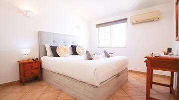 A bedroom with a bed, nightstand, lamp, and a window with an air conditioning unit.