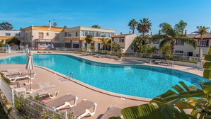 A swimming pool with lounge chairs and a building with a yellow and white facade. - Townhouse w/ Pool & Leisure in São Rafael (Albufeira)