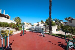 An outdoor gym with exercise equipment, a palm tree, and a white building with a dome in the background. - Townhouse w/ Pool & Leisure in São Rafael (Albufeira)