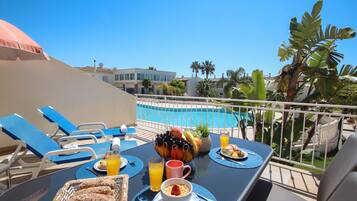 A dining table with breakfast items, a pool, and lounge chairs.