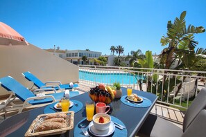 A dining table with breakfast items, a pool, and lounge chairs.