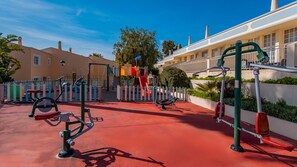 A playground with exercise equipment, a slide, and a building with balconies in the background. - Townhouse w/ Pool & Leisure in São Rafael (Albufeira)