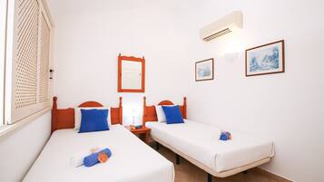 A hotel room with two beds, a window with a lattice design, a wall-mounted mirror, and two framed pictures.