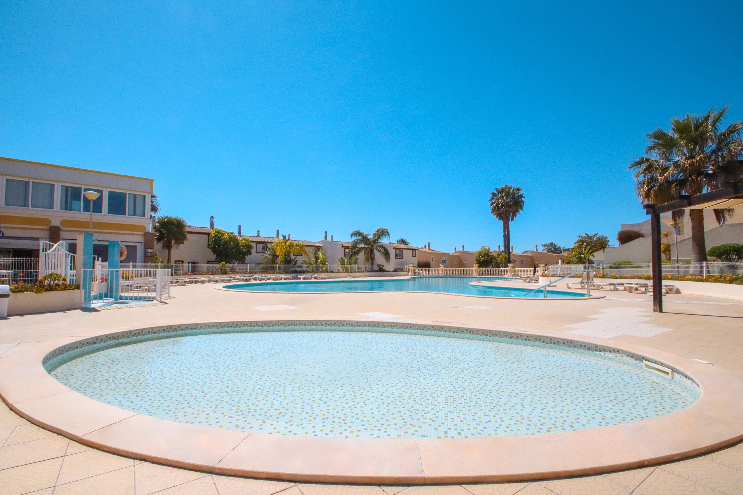 A pool area with multiple circular pools, palm trees, and a building with a yellow facade.