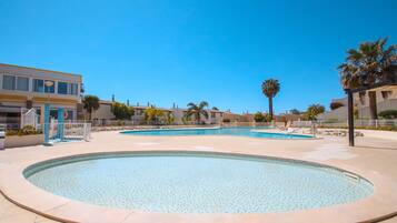 A pool area with multiple circular pools, palm trees, and a building with a yellow facade.