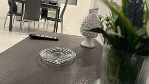 A dining area with a table, chairs, a remote control, and a decorative item. - Blue Heracleo Apartment center Trapani (Trapani)