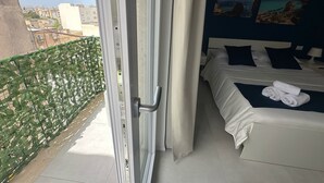 A hotel room with a bed, a nightstand, and a view of the cityscape through a balcony door. - Blue Heracleo Apartment center Trapani (Trapani)