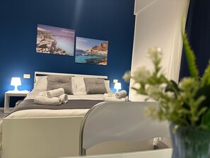 Habitación de hotel con cama, dos lámparas de noche, una mesita de noche y dos cuadros en la pared.