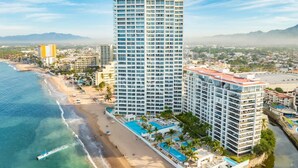 Un hotel de altura con múltiples balcones, ubicación frente a la playa y zona de piscina.