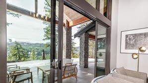 A modern interior with a glass door leading to an outdoor patio. Inside, there is a sofa and a dining table with chairs. - Sunset View Retreat: Theater & Hot Tub Suncadia (Cle Elum)