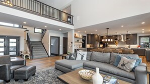 A spacious living area with a grey sectional sofa, a wooden coffee table, and a staircase leading to an upper level. - Sunset View Retreat: Theater & Hot Tub Suncadia (Cle Elum)