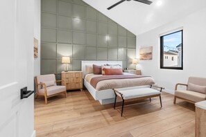 A modern bedroom with a large bed, two bedside tables, a bench, and a view of buildings through a window.