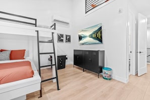 A bunk bed with a ladder, a desk with a chair, a black cabinet, a painting, and a door.