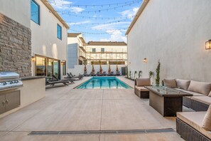 A backyard with a swimming pool, lounge chairs, a barbecue grill, and a glass-top table.