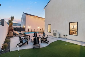 Een modern buitenterras met zwembad, omringd door ligstoelen en een verzorgd gazon.