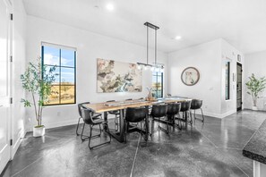 A modern kitchen with a large island, black chairs, and a view of the desert through the windows.
