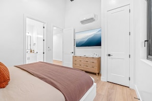 Een slaapkamer met een bed, een dressoir, een televisie en een badkamer die door een geopende deur zichtbaar is.