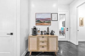 A hallway with a wooden cabinet featuring a coffee machine, a framed landscape painting, and a schematic drawing on the wall.