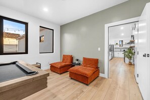 A modern living room with a pool table, two orange sofas, and a view of the outside through a large window.
