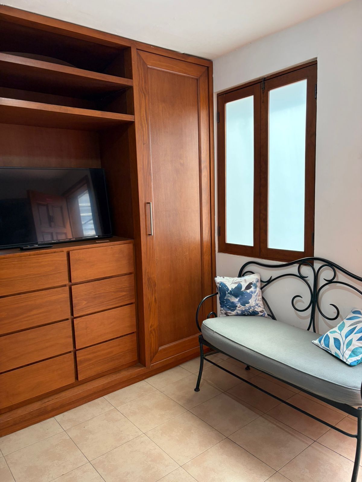 A room with a wooden wardrobe, a bench with cushions, and a window with a view.