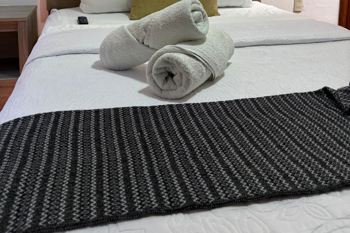 A neatly made bed with white linens, a brown headboard, and a patterned throw blanket.