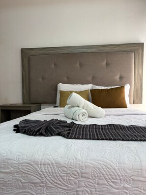 A neatly made bed with a white quilt, two pillows, and a rolled towel. - CASARU HOTEL OAXACA CENTRO (Oaxaca)
