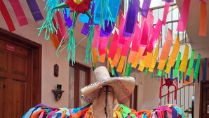 Une pièce décorée de motifs colorés en papier suspendus au plafond, avec une porte en bois, un banc en métal et un canapé gris.