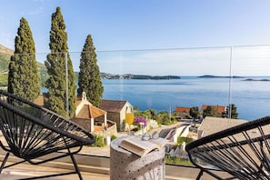 Relax on the balcony with a serene sea view, surrounded by cypress trees and a distant island.