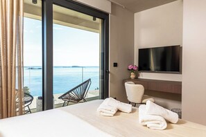 Enjoy a serene sea view from the balcony, featuring a flat-screen TV, comfortable seating, and a well-appointed bed.