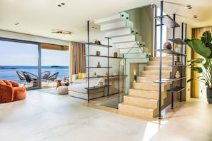 Stunning staircase leads to a cozy seating area with a sofa and chairs, offering a view of the sea.