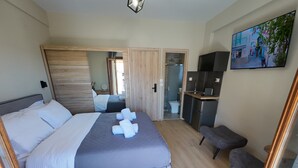 A modern hotel room with a large bed, a small desk, a chair, and a bathroom visible through an open door. - Nel Paese Room (Skiathos)