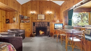 Een knus blokhutinterieur met een stenen openhaard, houten wanden, een eethoek en een boekenkast.