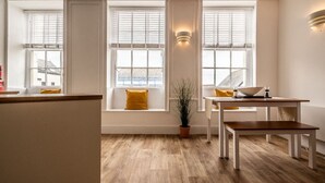 A modern kitchen with a wooden floor, white cabinetry, a dining table with chairs, and a window with a view. - Stylish and bright City Centre apartment (Exeter)