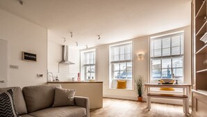 A modern living room with a sofa, a small table, and a kitchen area with a window. - Stylish and bright City Centre apartment (Exeter)