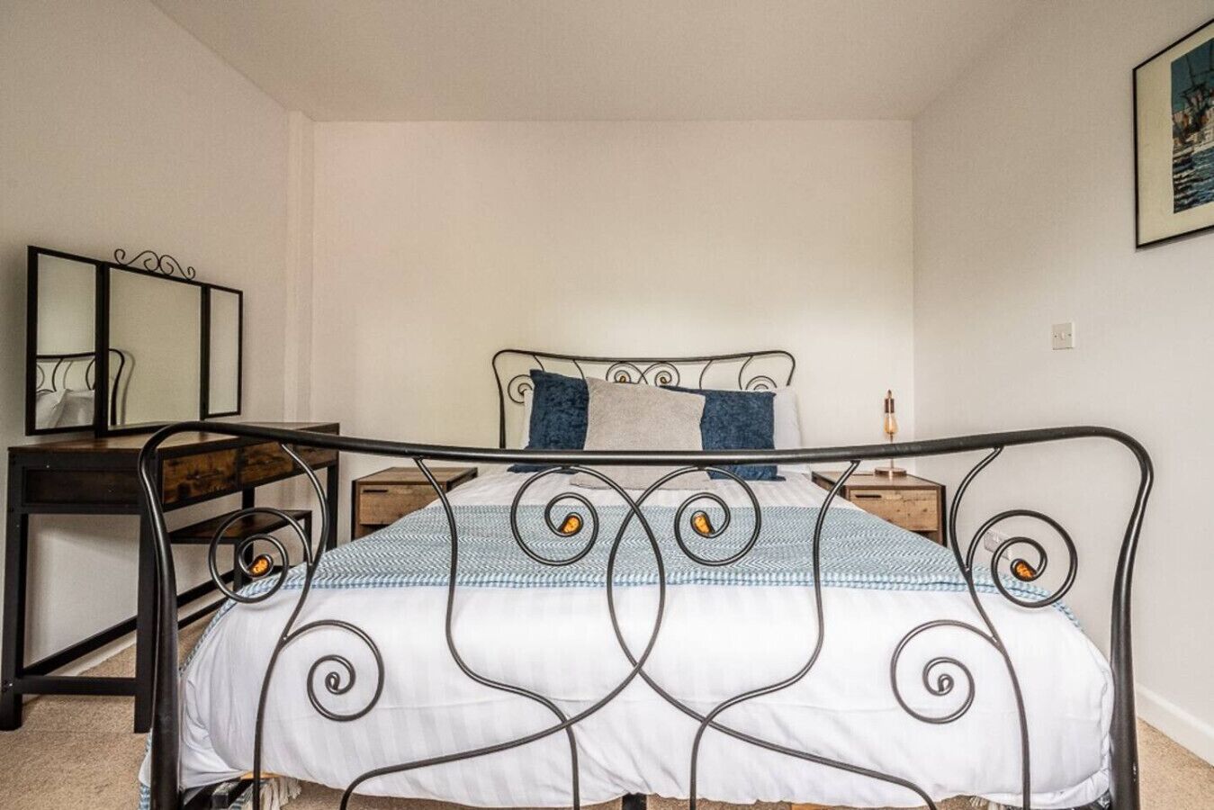 Une chambre à coucher avec un lit en métal, une table de chevet, une chaise et un miroir au mur.