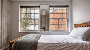 A bedroom with a bed, two windows, a wooden headboard, and a brick wall visible through the windows.