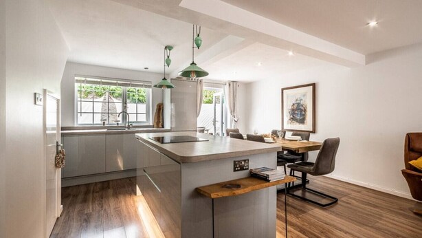 A modern kitchen with a central island, pendant lighting, and a dining area with a table and chairs.