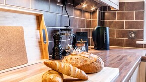 A kitchen with a wooden countertop, a loaf of bread, a croissant, a coffee maker, and a pepper grinder. - Stylish townhouse by the Quay with parking (Exeter)