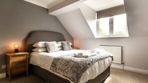 A bedroom with a sloped ceiling, a bed with a grey headboard, a bedside table with a lamp, and a window with daylight. - Stylish townhouse by the Quay with parking (Exeter)
