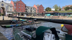A marina with boats docked, a covered seating area, and buildings in the background. - Stylish townhouse by the Quay with parking (Exeter)