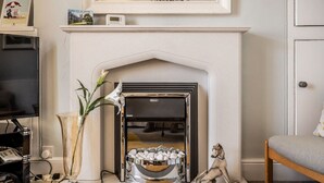 A living room with a fireplace, a vase with flowers, a decorative dog statue, and a television. - Charming character lodge in cemetery grounds (Devon)