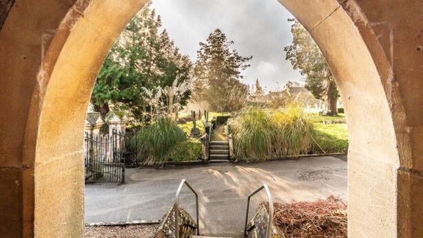 An arched entrance to a cemetery with a pathway leading to a gate. - Charming character lodge in cemetery grounds (Devon)
